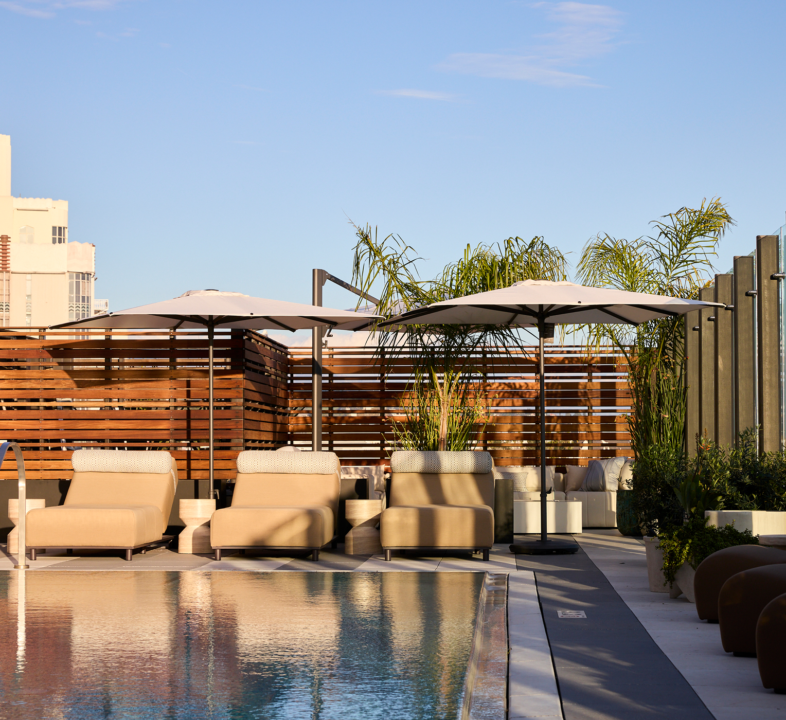 Rooftop swimming pool with lounge seating, cabanas, and city views under blue sky