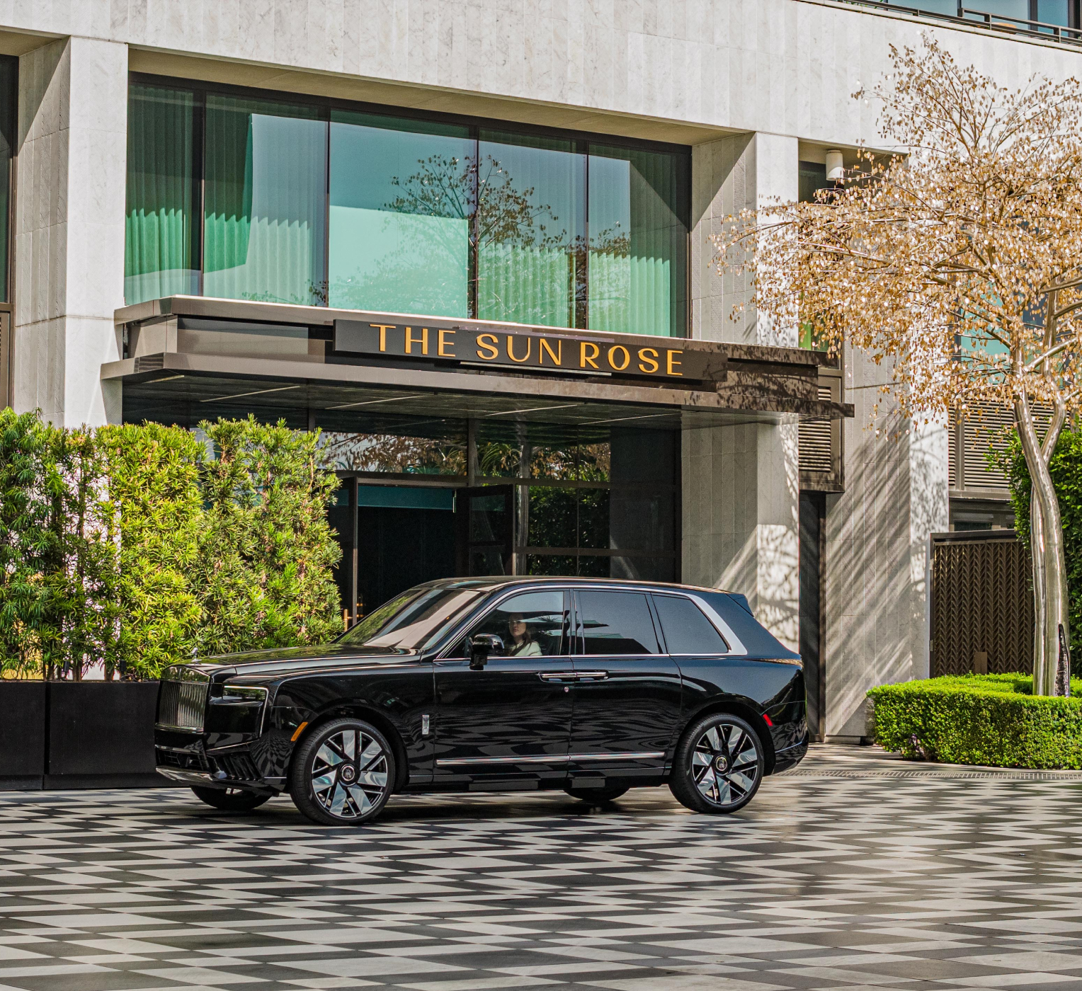 Luxury SUV parked at The Sun Rose Hotel entrance with modern facade and greenery