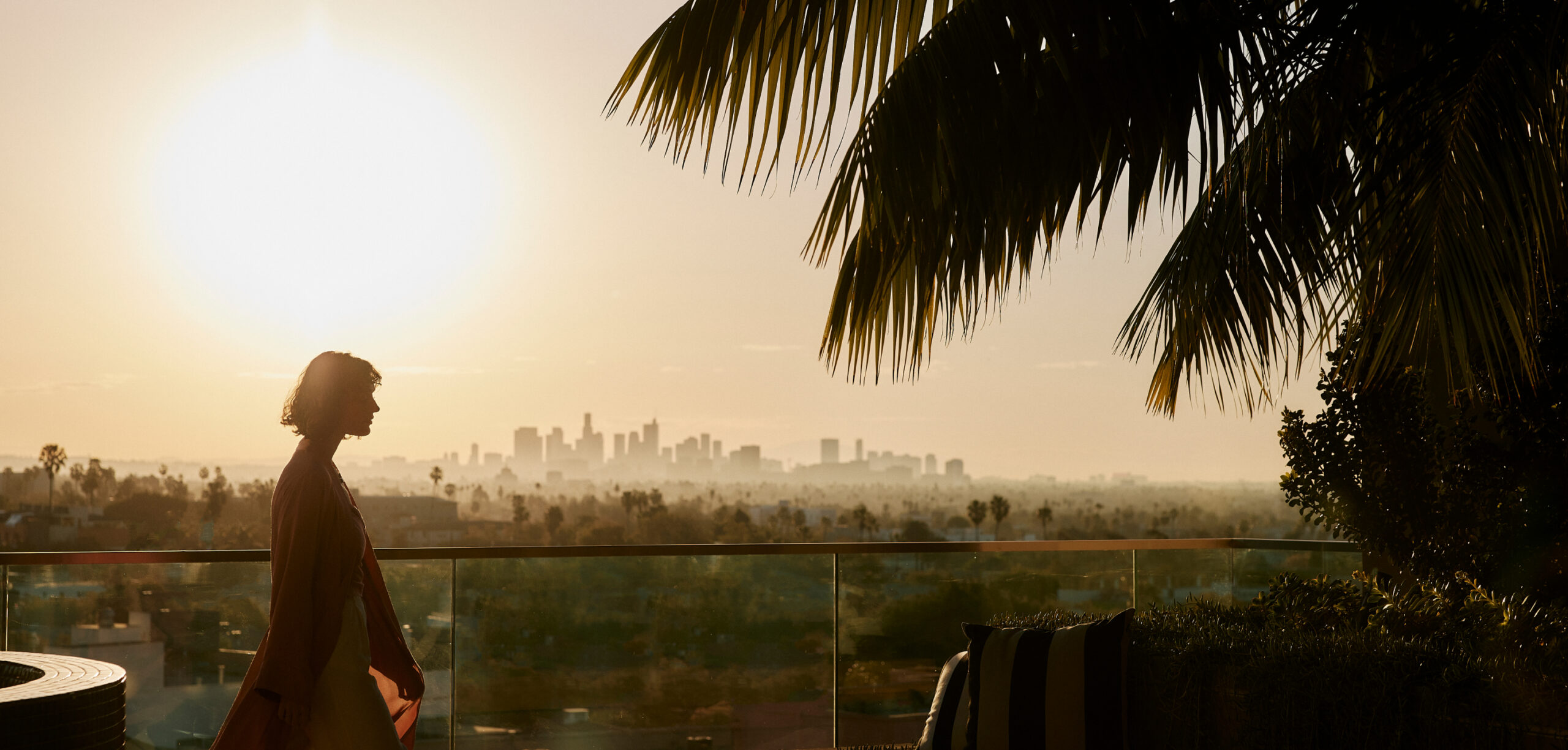 Silhouette of a woman walking on a balcony overlooking a city skyline at sunset